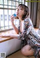 A woman sitting on a window sill drinking from a cup.