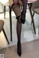 A woman in black stockings and high heels sitting at a table.