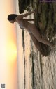 A woman in a bikini standing on a rock by the ocean.